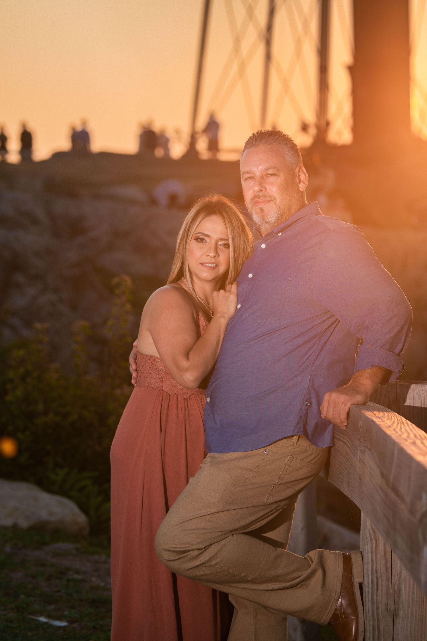 Romantic couple sits together on a wooden bench during golden hour sunset at a coastal overlook.