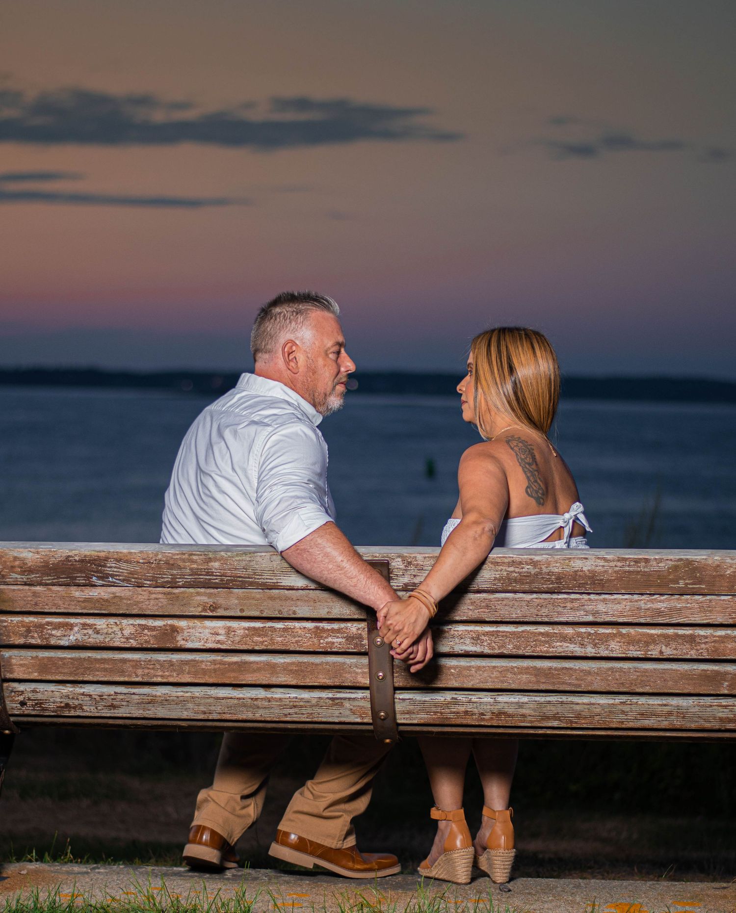 Couple shares tender moment on wooden bench overlooking scenic ocean sunset view.