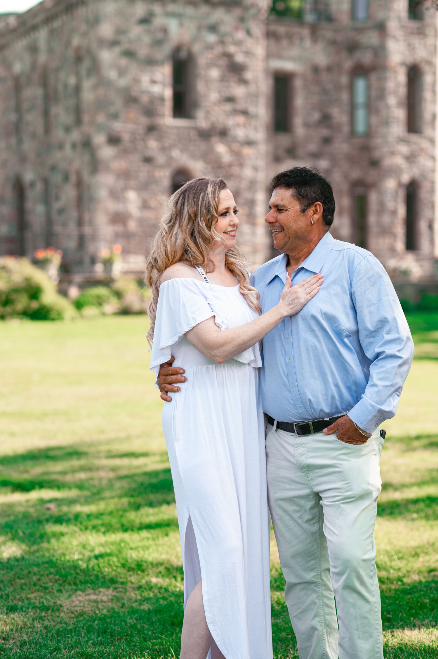 Engagement photos of couple in light blue and white clothing near historic stone building.