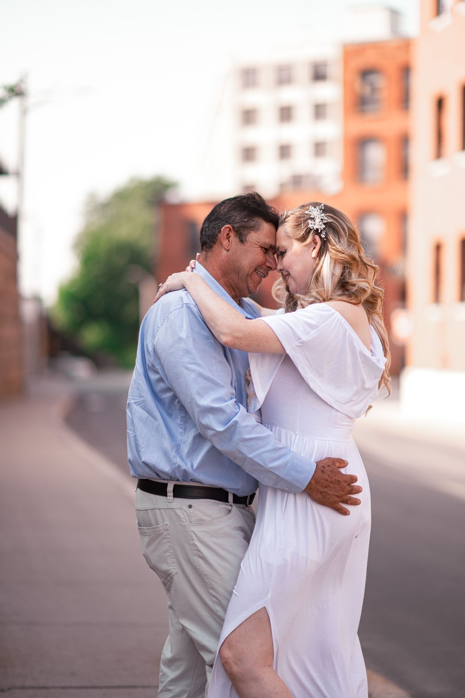 A romantic couple embraces in an urban setting, with brick buildings in the background.