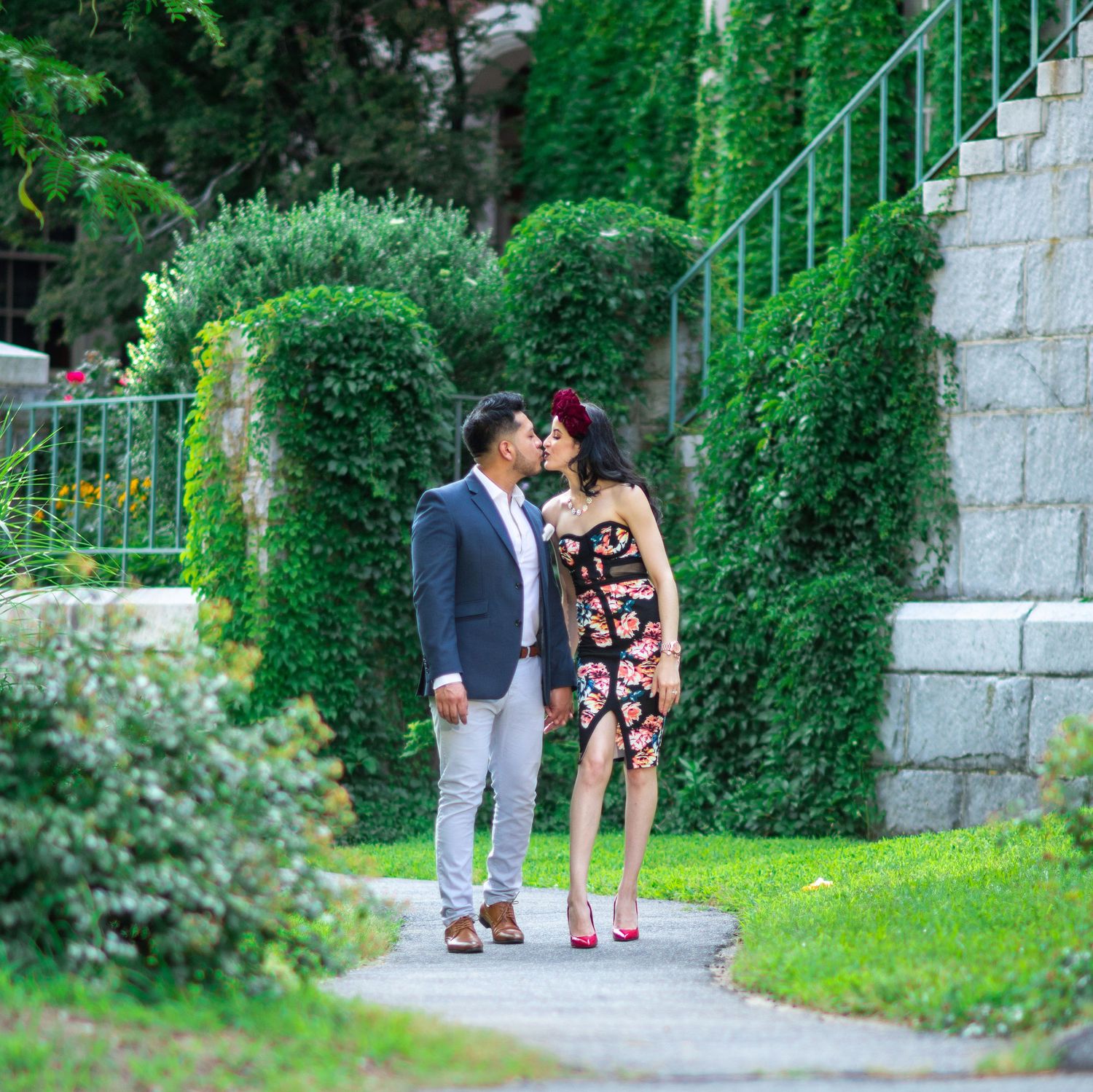 Romantic couple embracing on garden path surrounded by lush greenery and stone steps.