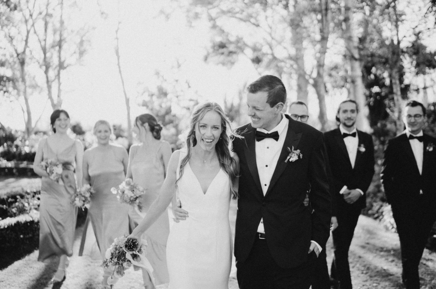 bride and groom laughing with bridal party in background
