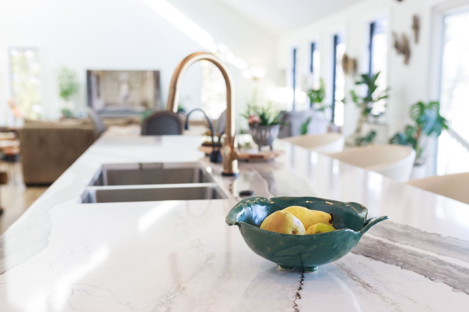 Clean white marble kitchen counter with teal bowl and copper faucet in natural light.