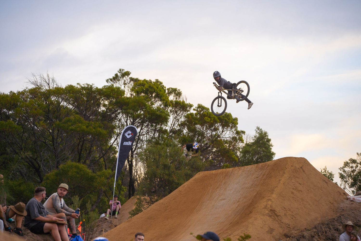 BMX rider performing high-flying aerial stunt over dirt jump at sunset.