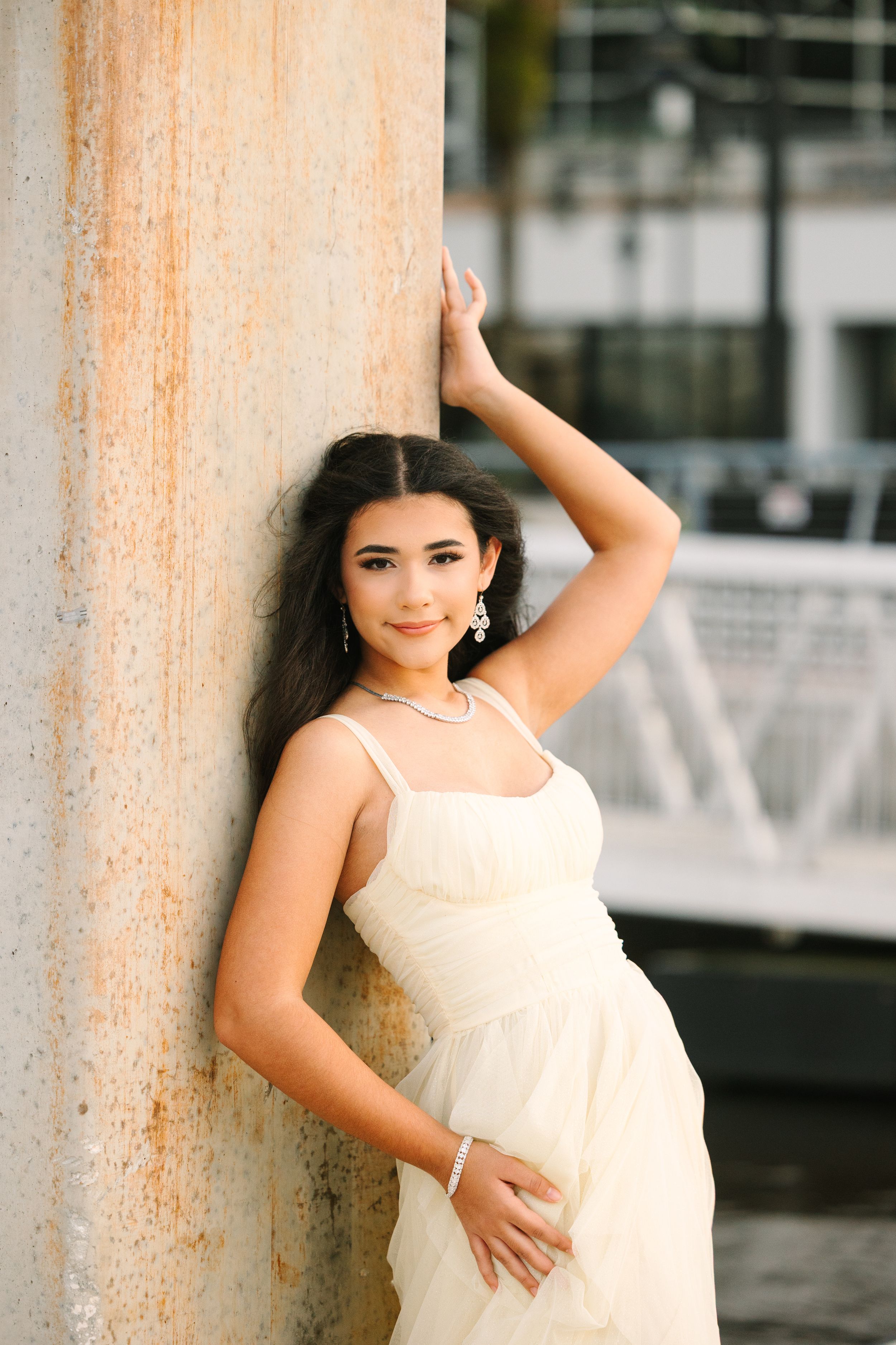 Quinceañera in cream-colored dress poses against a rustic pillar in an outdoor portrait series.