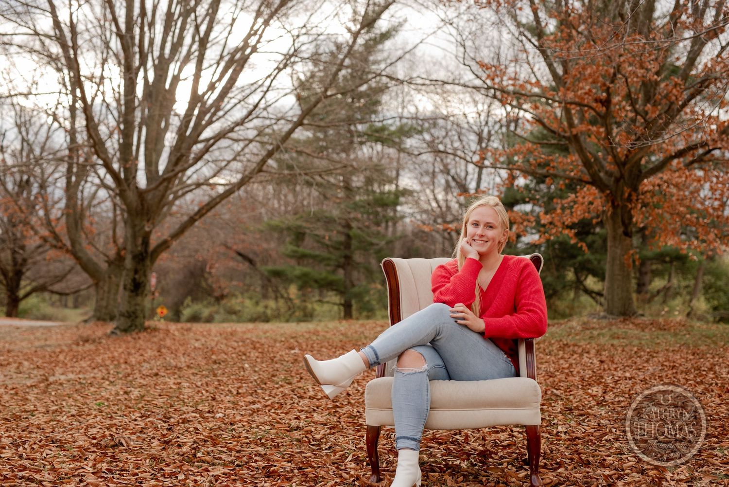 Casual autumn portrait in a beige armchair surrounded by fallen leaves.