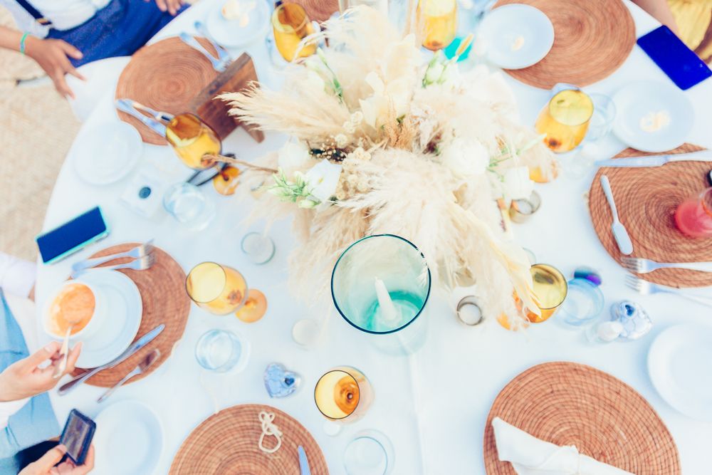 Overhead view of beach wedding reception table with woven placemats and tropical centerpiece.