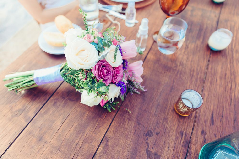 Colorful bridal bouquet with pink and purple flowers resting on rustic wooden table.