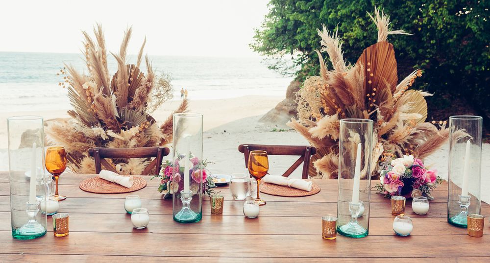 Coastal wedding table setting with dried pampas grass centerpieces and turquoise glass accents.