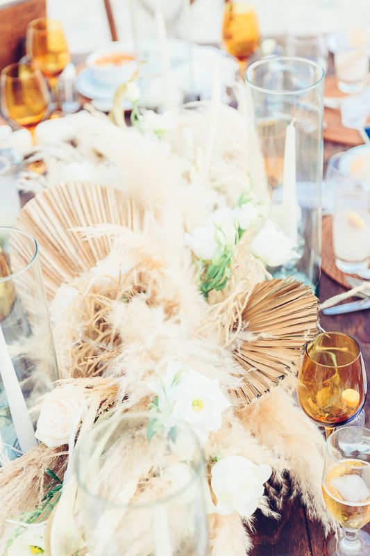 Wedding table decor with dried palm fronds, white flowers and amber glassware.