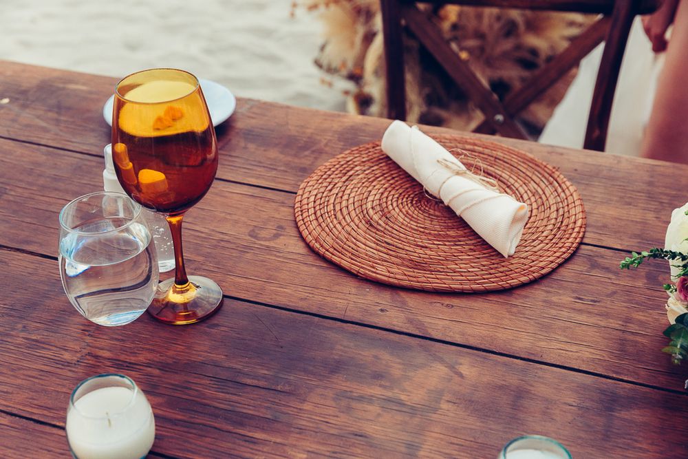 Elegant place setting with amber wine glass and woven placemat on wooden table.