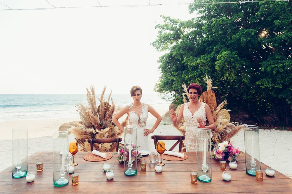 Beachfront wedding bar setup with bohemian dried flower arrangements and colorful glassware.