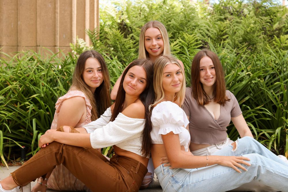Group of friends in light colored outfits pose together on garden steps.