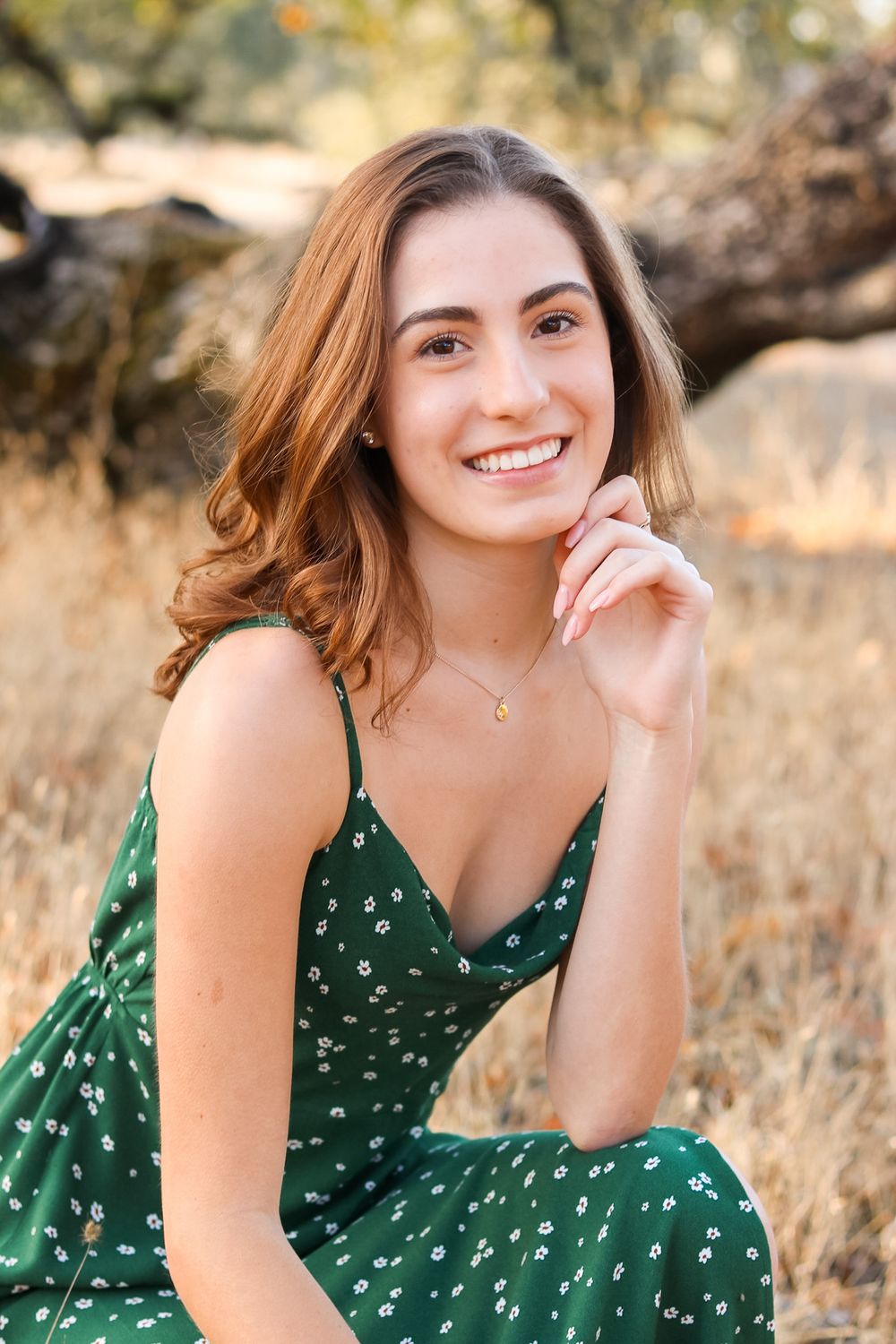Woman in green polka dot dress poses in golden field during sunset.