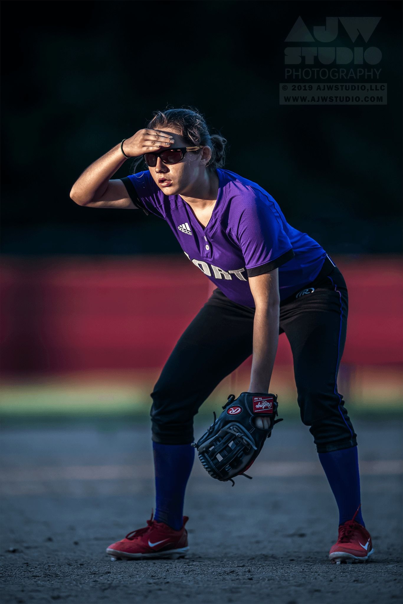 Softball player in purple uniform crouching in ready position on field.