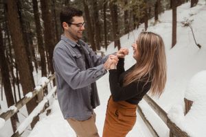 A playful winter engagement photoshoot on a snowy forest path.