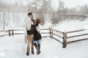 A couple dancing together on a snowy winter day by a rustic fence.