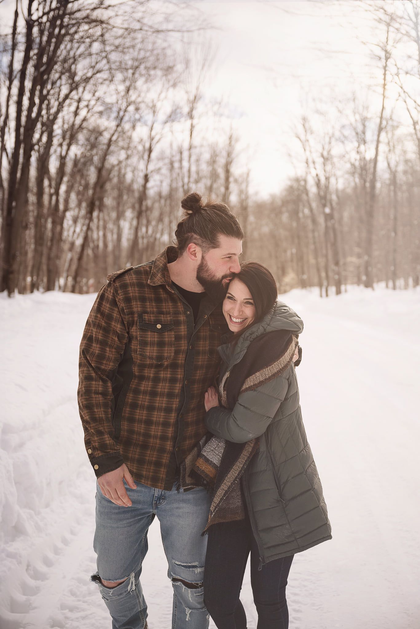 A couple embracing on a snowy winter trail wearing casual outerwear.