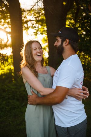 A joyful couple sharing a laugh at sunset in a wooded setting.