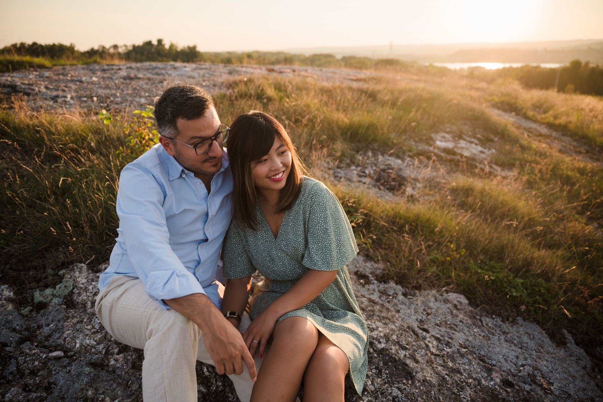 A couple sitting on rocky terrain at sunset sharing an intimate moment.