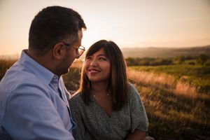 Romantic couple sharing tender moment in golden sunset field with mountain backdrop.