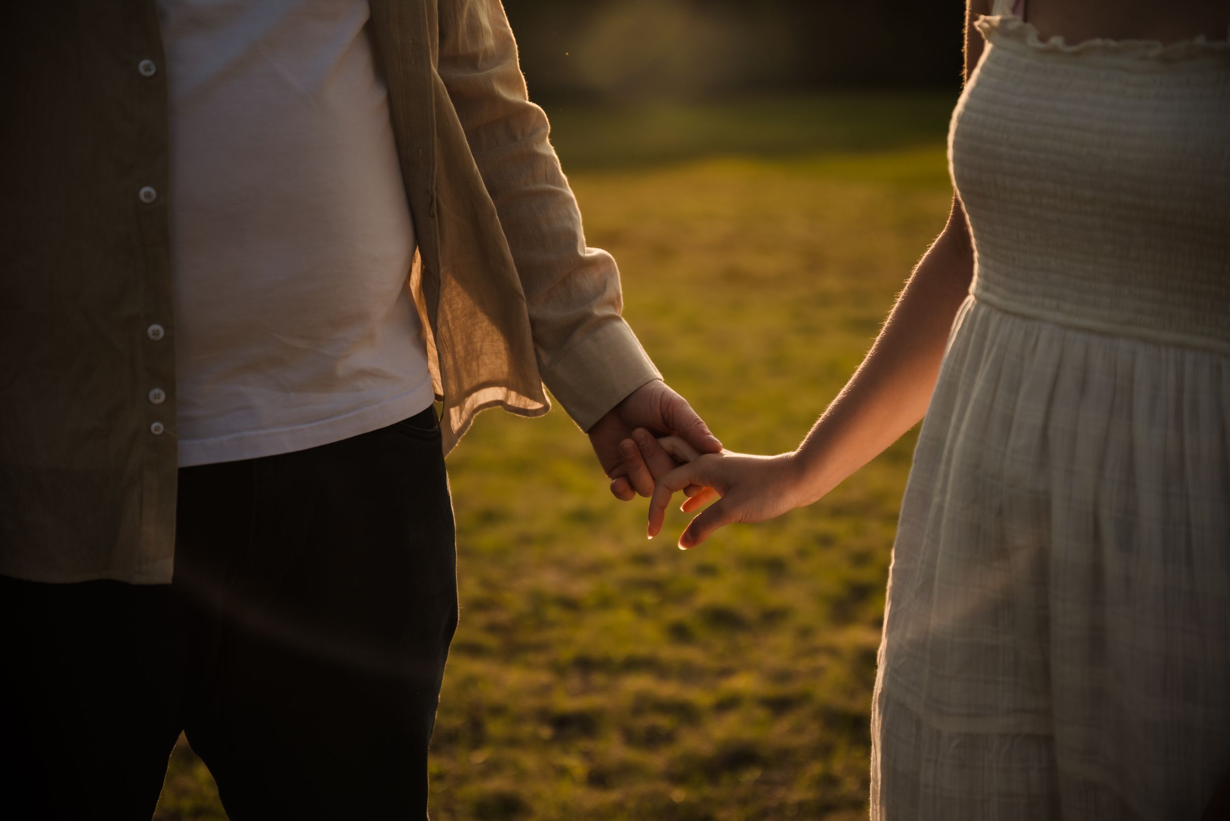 A close-up shot of two people holding hands in warm sunset lighting.