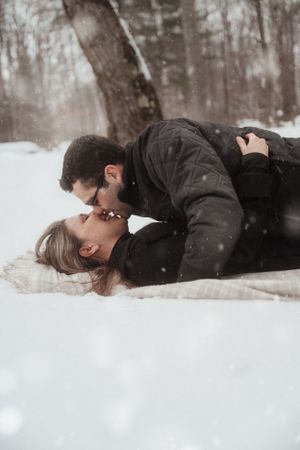A romantic winter scene showing a couple lying in the snow during snowfall.