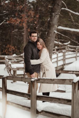A romantic winter portrait of a couple embracing on a snow-covered wooden bridge.