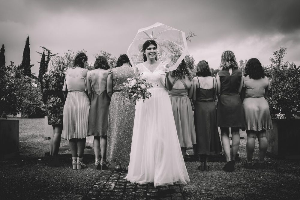 Black and white photo of wedding party with bridesmaid dresses and white umbrella outdoors.