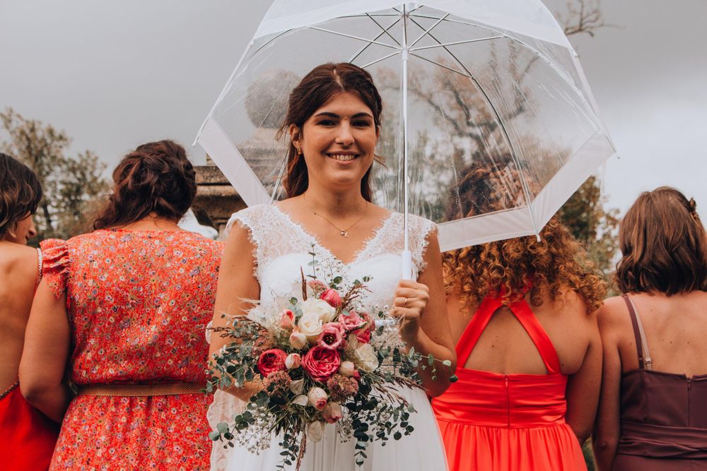 Wedding party member holding clear umbrella and pink bouquet in colorful dress lineup.