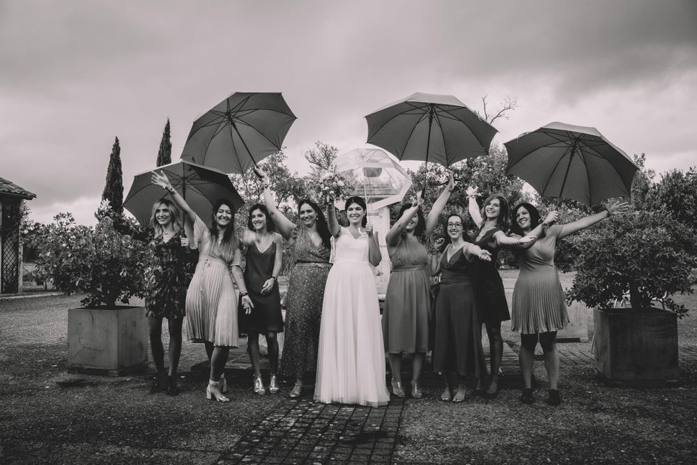 Wedding party posing with umbrellas in black and white photograph outdoors.