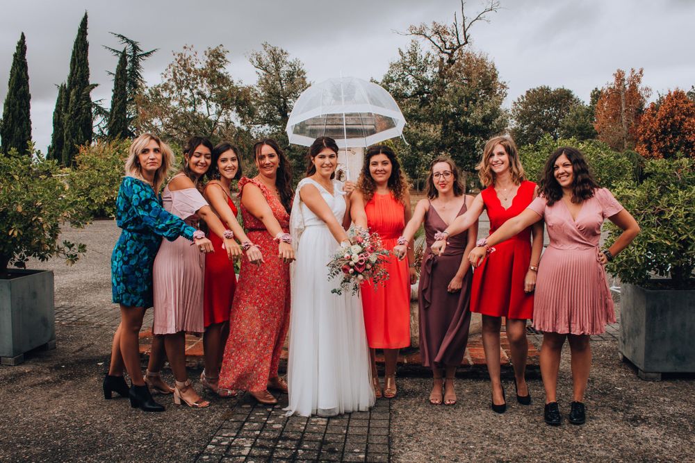 Wedding party in colorful dresses posing together in garden setting with cypress trees.