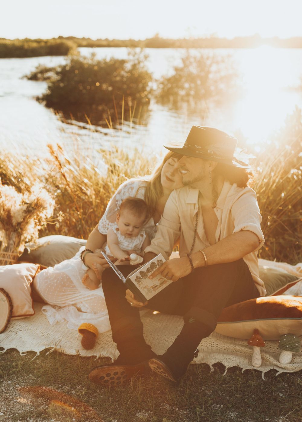 Parent and child reading book together by lakeside during sunset.