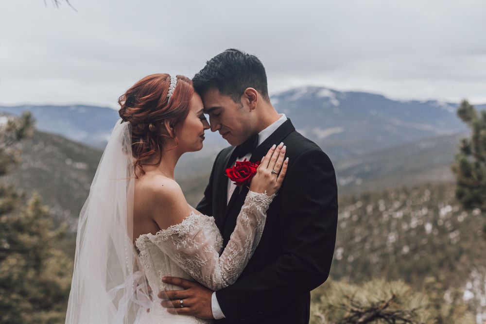 Bride and groom share intimate moment against mountain landscape backdrop.