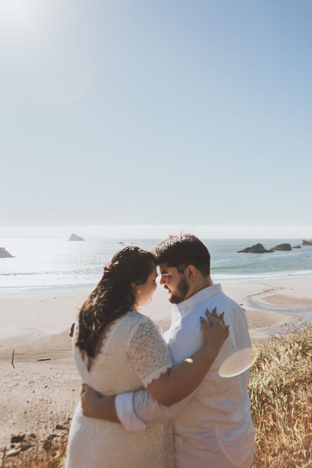 Couple embraces on coastal clifftop overlooking ocean during golden hour.