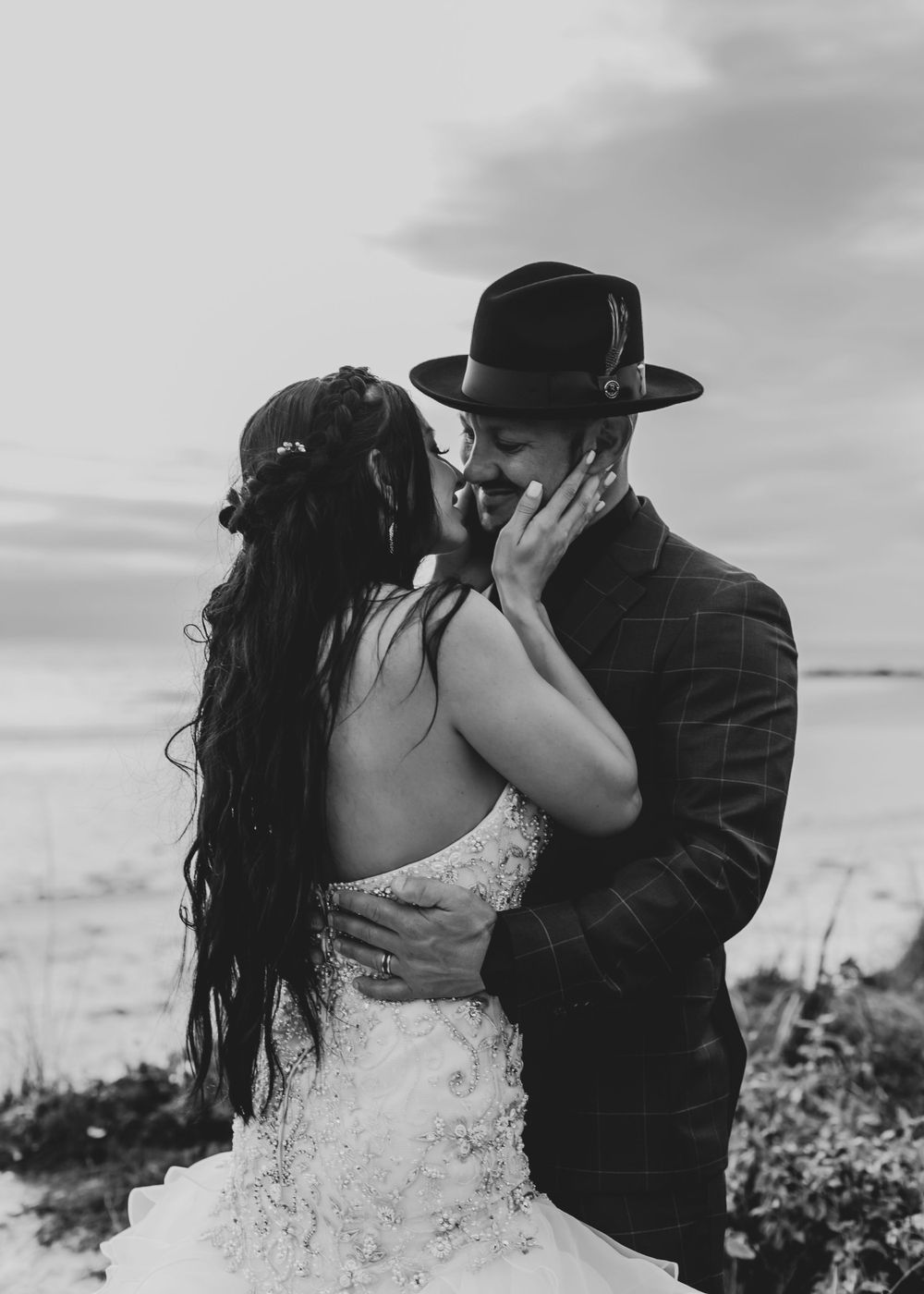 Intimate black and white portrait of couple kissing on beach with dramatic lighting.