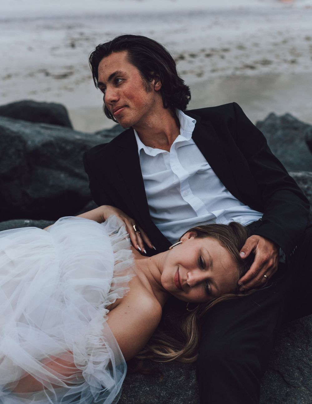 Intimate moment between couple on rocky beach with dramatic moody lighting.
