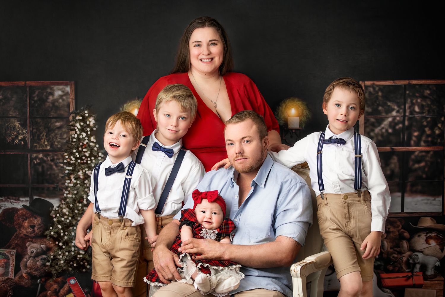 Family portrait with coordinated outfits featuring suspenders and red accents against Christmas backdrop.