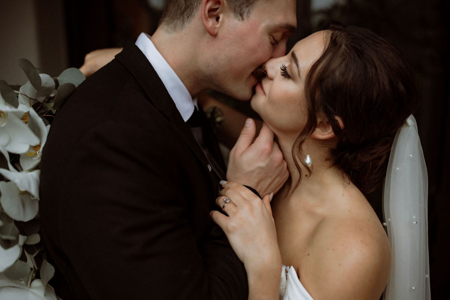 An intimate moment between newlyweds sharing a tender kiss against a floral backdrop.