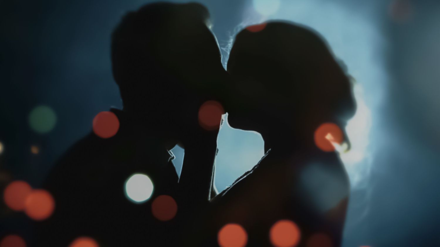 Silhouetted couple kissing against a blue background with bokeh lights.