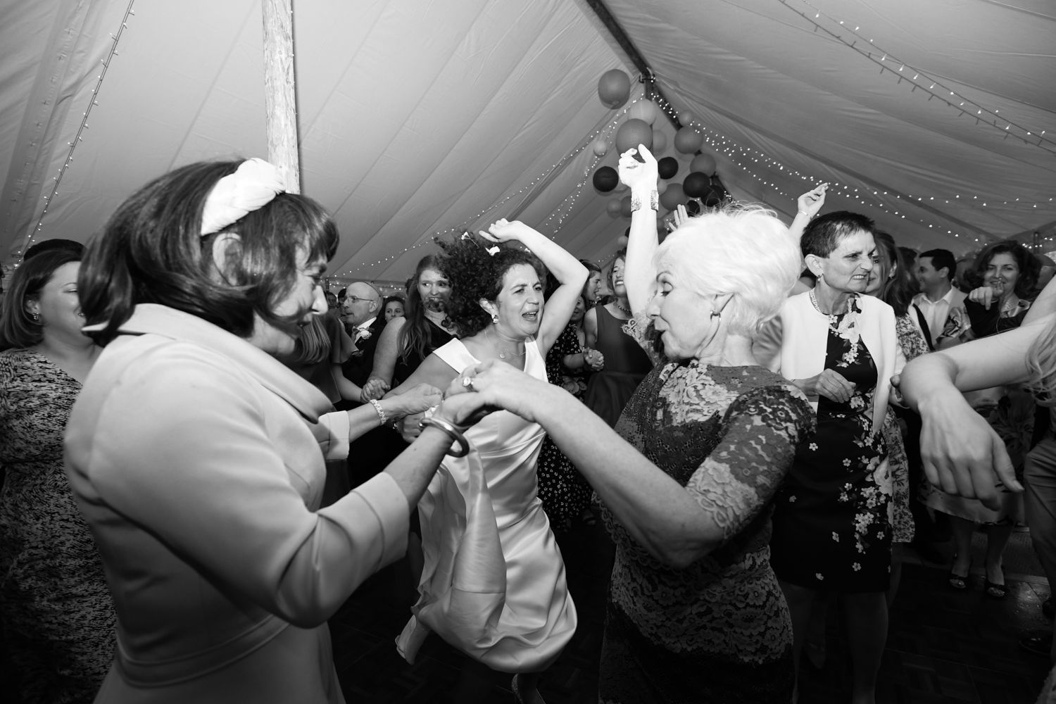 Energetic dancing and celebration at wedding reception under white tent.