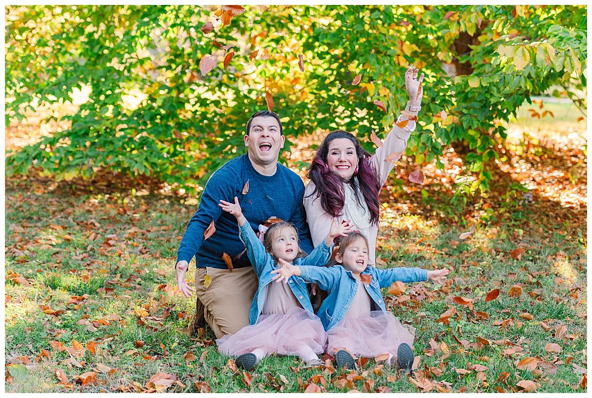 Family portrait photographer captures twins mom dad throwing fall leaves in autumn