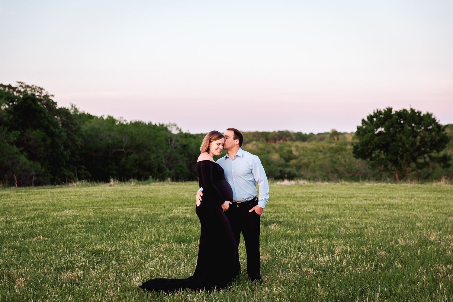 couple shares a tender kiss in an open green field