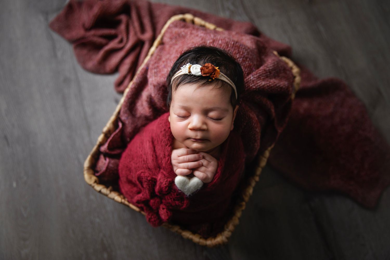 Overhead view of sleeping newborn on burgundy blanket with decorative trim.