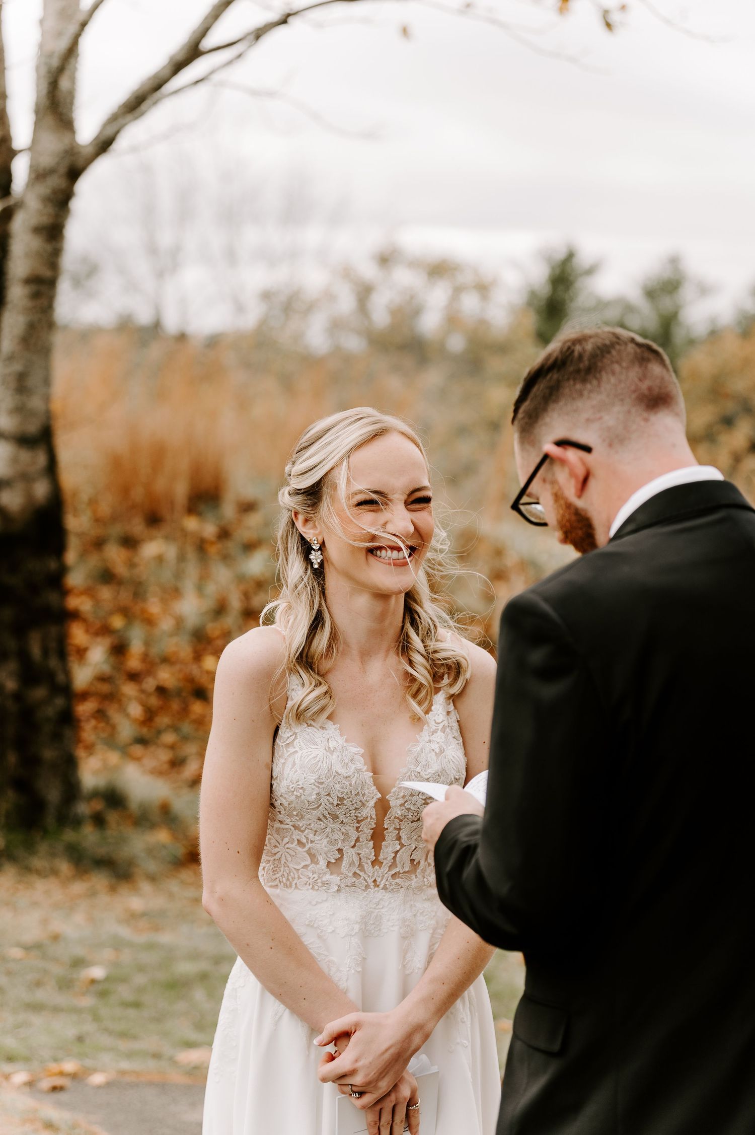 A couple shares a joyful moment during their first look on a path surrounded by autumn foliage.