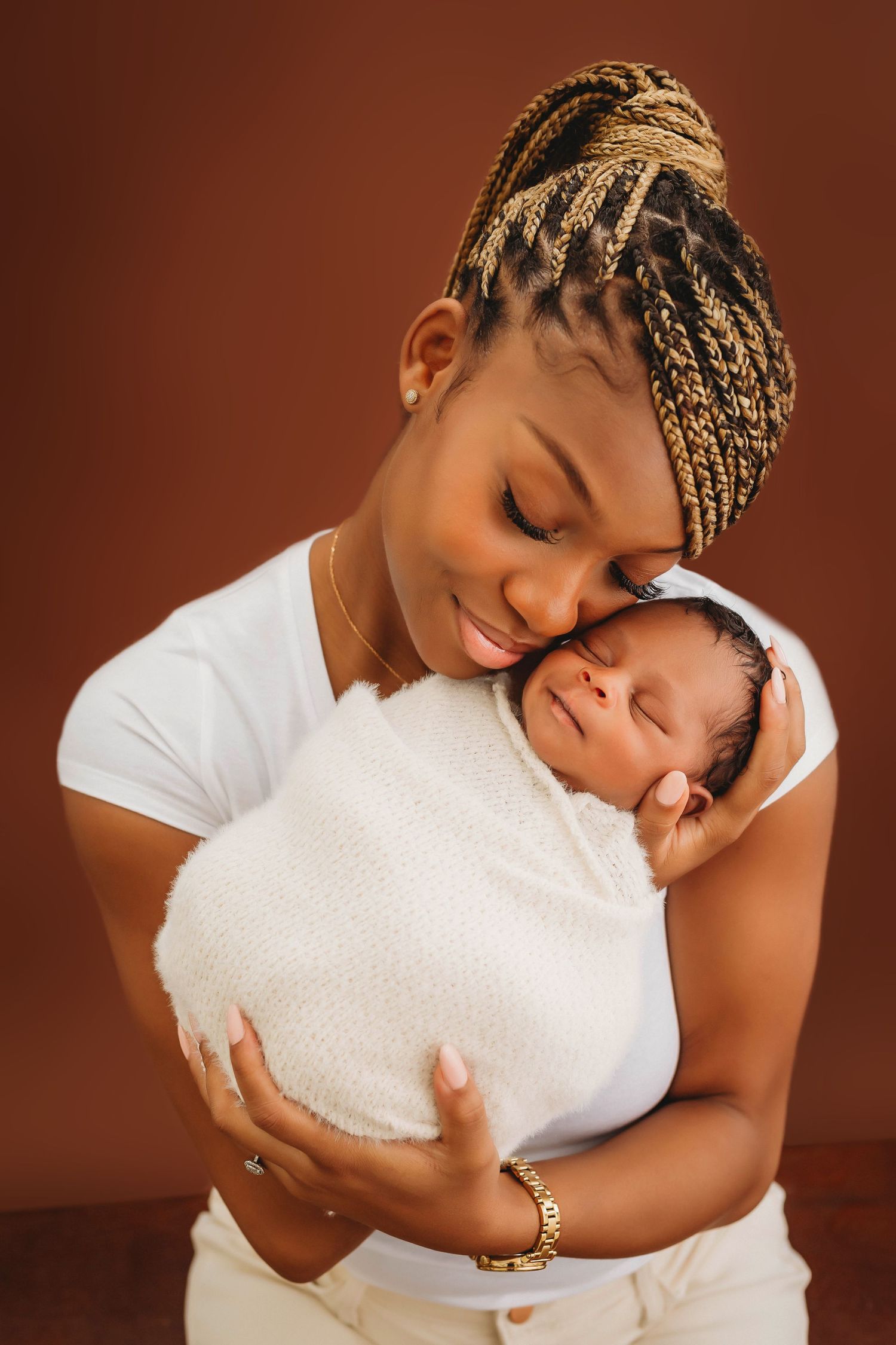 Tender moment between parent and newborn swaddled in white against warm brown background.