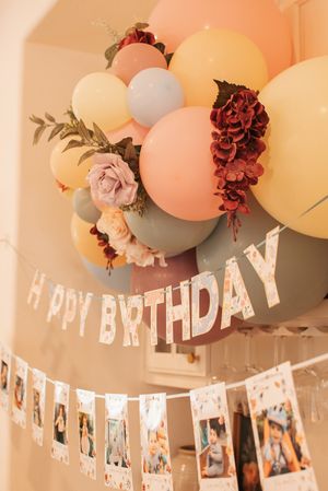 Birthday party decorations featuring pastel balloon arch with roses and photo garland.