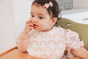 Toddler wearing a rainbow bib and floral dress at mealtime.