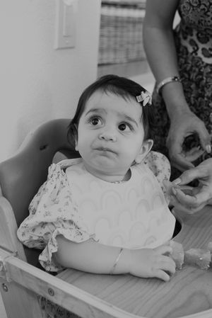 A young toddler in a floral dress sitting in a high chair with a sweet expression.
