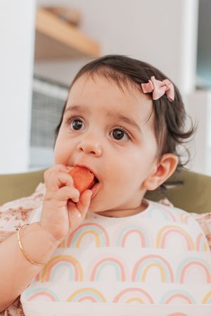 Small child eating a strawberry while wearing a rainbow-patterned bib.